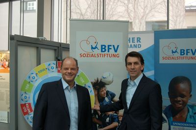 Schatzmeister Jürgen Faltenbacher und BFV-Geschäftsführer Jürgen Igelspacher posieren am Stand der BFV-Sozialstiftung mit Roll-Ups und Glücksrad beim Münchner Stiftungsfrühling