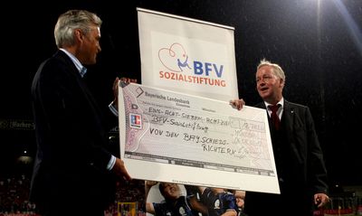 Mittelalter Mann aus dem Schiedsrichterbereich übergibt einen Spendenscheck an den Stiftungsvorstand der BFV-Sozialstiftung, Prof. Dr. Manfred Heim