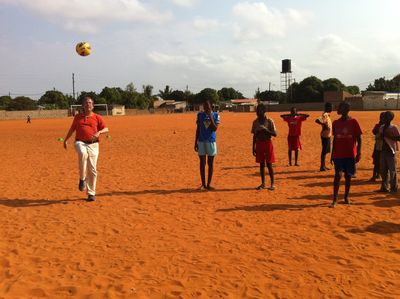 Koch jongliert Fußball auf Sportplatz in Albazine; sieben mosambikanische Jugendliche als Zuschauer